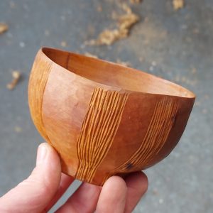 A hand holding a small, carved wooden bowl. Grooved patterns decorate the outside.